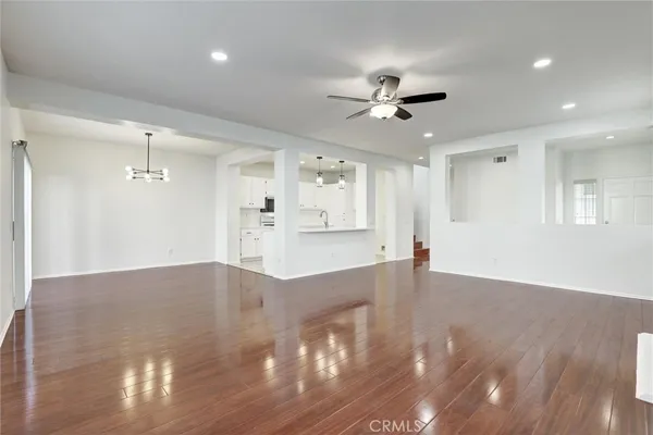 a view of an empty room with wooden floor and a ceiling fan