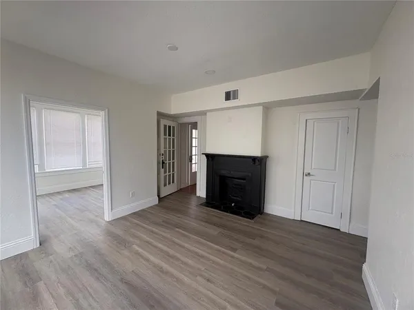 a view of an empty room with wooden floor fireplace and a window