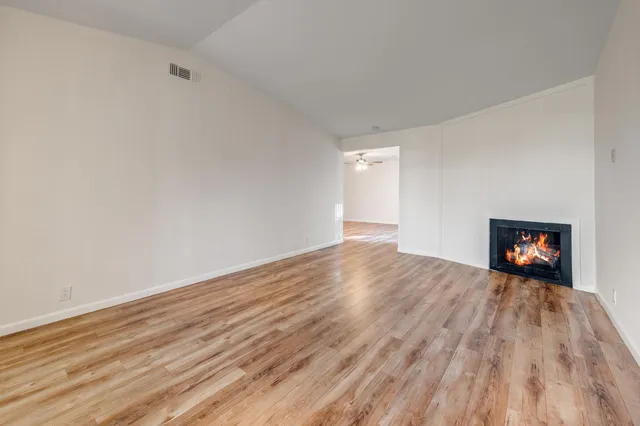 a view of an empty room with wooden floor and a fireplace