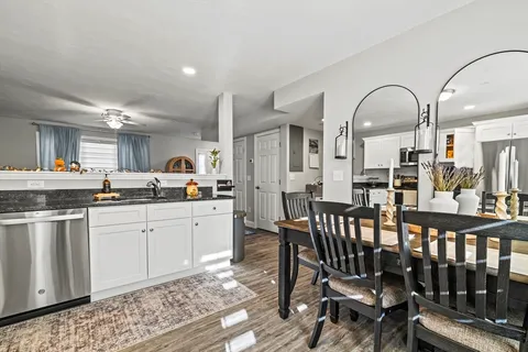 a open kitchen with stainless steel appliances granite countertop a dining table chairs sink and white cabinets