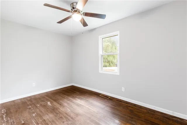 an empty room with wooden floor fan and windows