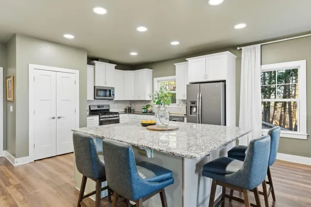 a kitchen with stainless steel appliances granite countertop a dining table chairs refrigerator and cabinets