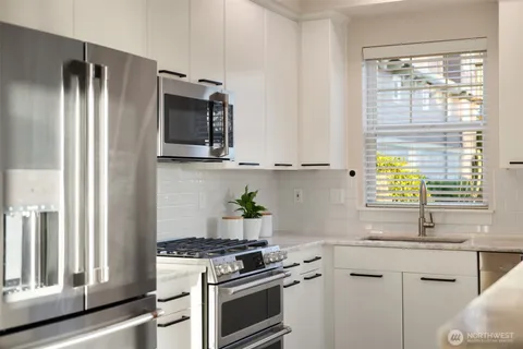 a kitchen with stainless steel appliances granite countertop white cabinets and a window