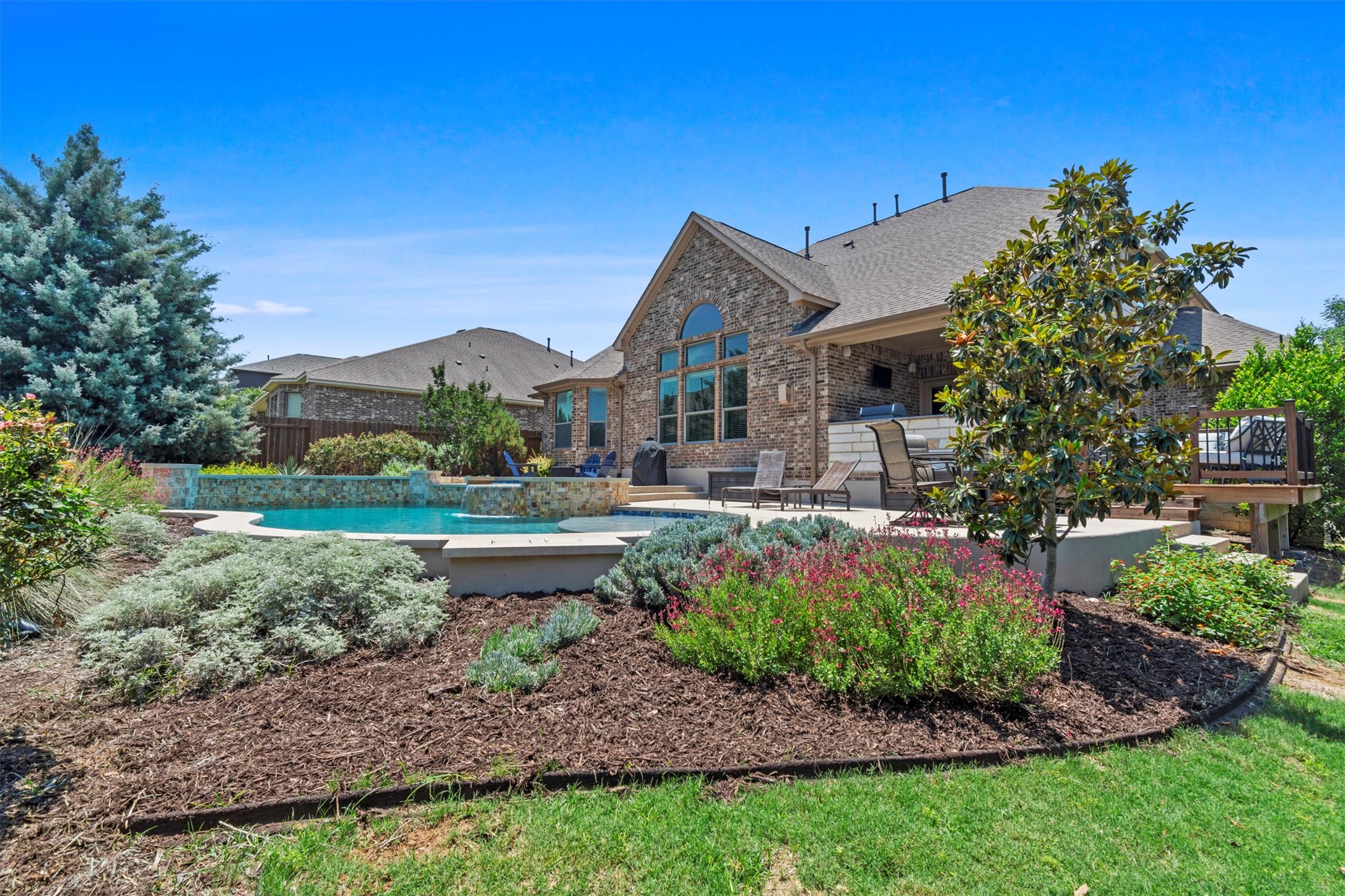 The backyard oasis you've been dreaming of—sparkling pool with a waterfall spa, lush landscaping, and room to lounge.
