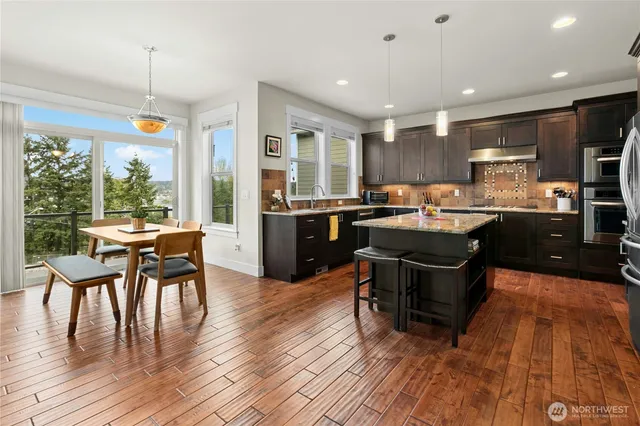 a kitchen with stainless steel appliances granite countertop a stove top oven a sink dishwasher a dining table and chairs with wooden floor