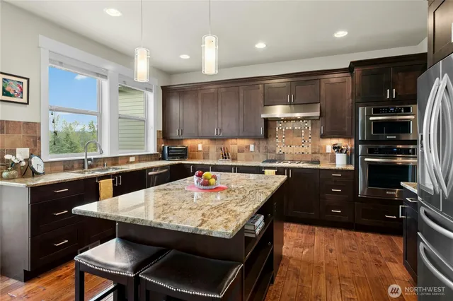 a kitchen with stainless steel appliances granite countertop a stove top oven a sink a dining table and chairs