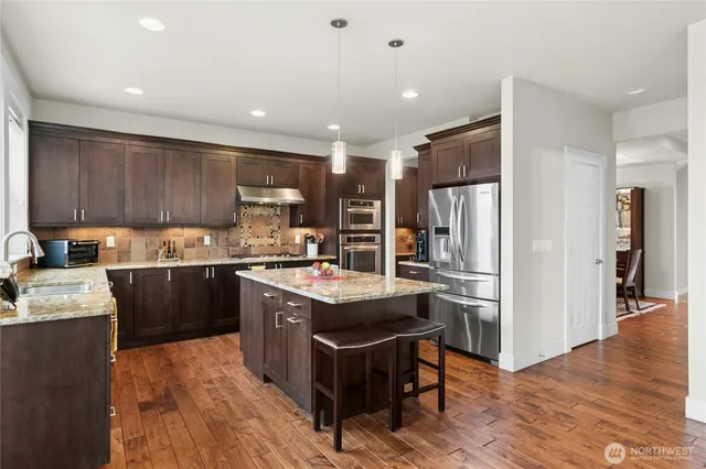 a kitchen with stainless steel appliances granite countertop a refrigerator a sink dishwasher a stove and white countertops with wooden floor