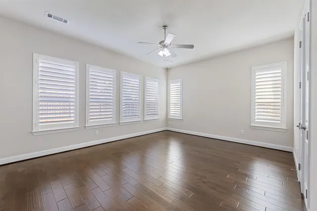 an empty room with wooden floor chandelier fan and windows