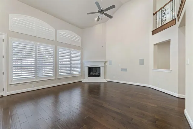 an empty room with wooden floor a ceiling fan and windows