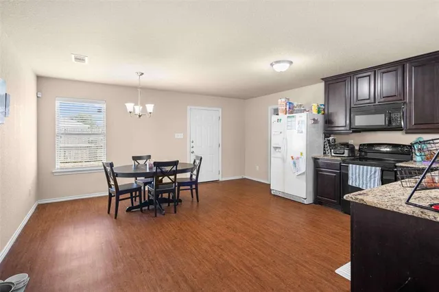 a kitchen with stainless steel appliances granite countertop a stove top oven a sink dishwasher a dining table and chairs with wooden floor