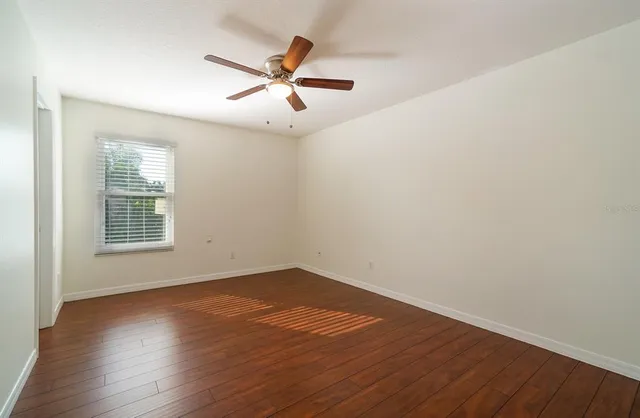 an empty room with wooden floor fan and windows