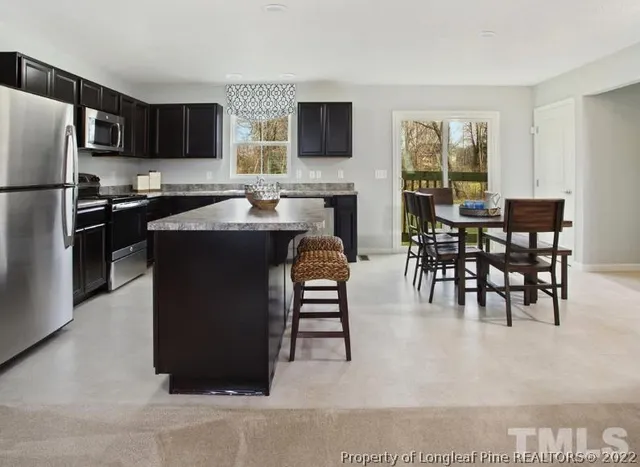 a living room with stainless steel appliances kitchen island granite countertop a refrigerator a stove a microwave a dining table and chairs