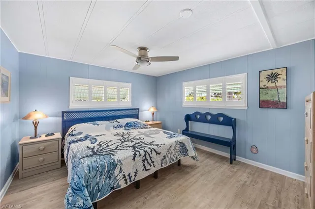 a bedroom with a bed and a lamp on dresser with wooden floor