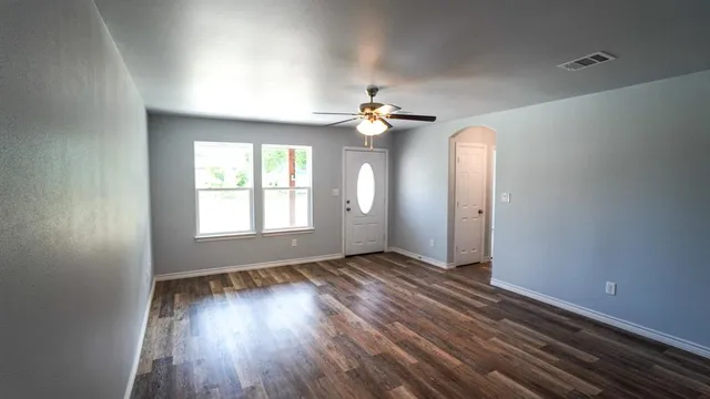 an empty room with wooden floor chandelier fan and windows