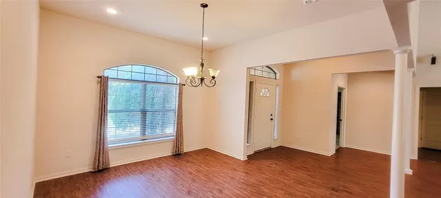 an empty room with wooden floor chandelier and glass door