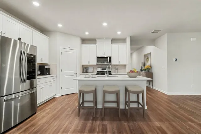 a kitchen with stainless steel appliances a microwave a stove a sink a refrigerator and chairs