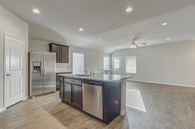 a kitchen with stainless steel appliances granite countertop a stove a refrigerator and a sink with wooden floor