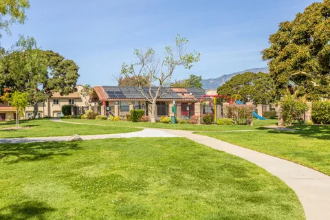 a view of a white house with a big yard and potted plants and large trees