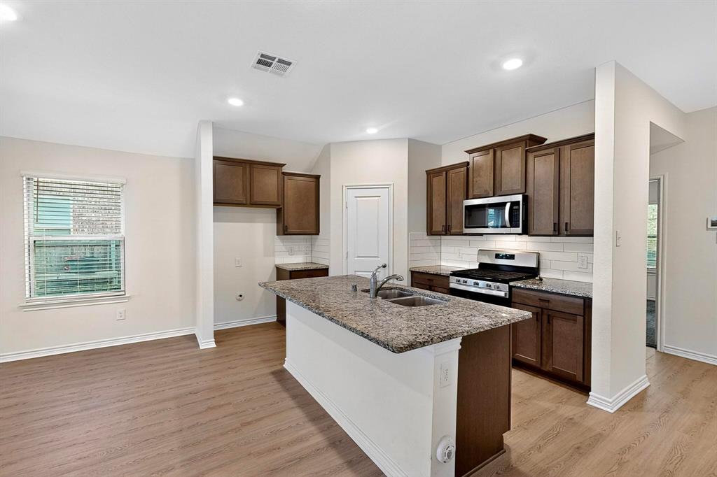 408 Rawhide Way Princeton, TX 75407 - Photo 10 of 36 a kitchen with stainless steel appliances granite countertop a stove top oven a sink dishwasher a refrigerator and a oven with wooden floor