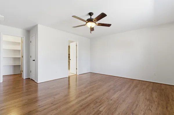an empty room with wooden floor a ceiling fan and windows