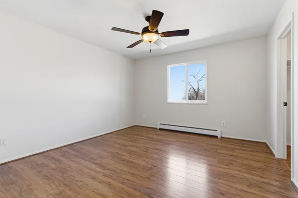 an empty room with wooden floor chandelier fan and windows