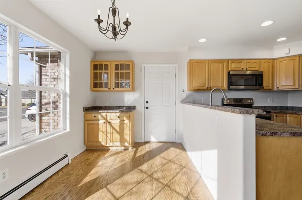 a kitchen with stainless steel appliances granite countertop a stove a sink a microwave a refrigerator a white cabinets and couches with wooden floor