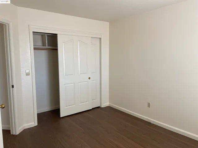 a view of an empty room with wooden floor and closet