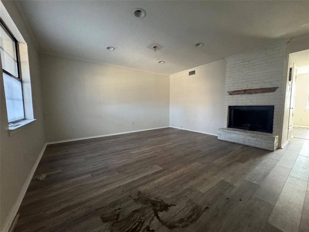 an empty room with wooden floor fire place and windows