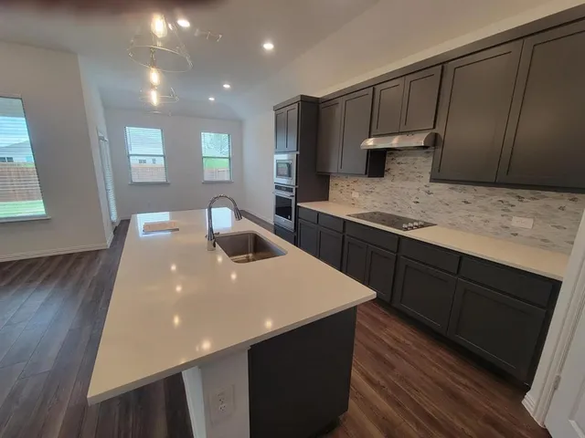 a kitchen with stainless steel appliances a sink dishwasher a stove a refrigerator a sink and dishwasher with wooden floor