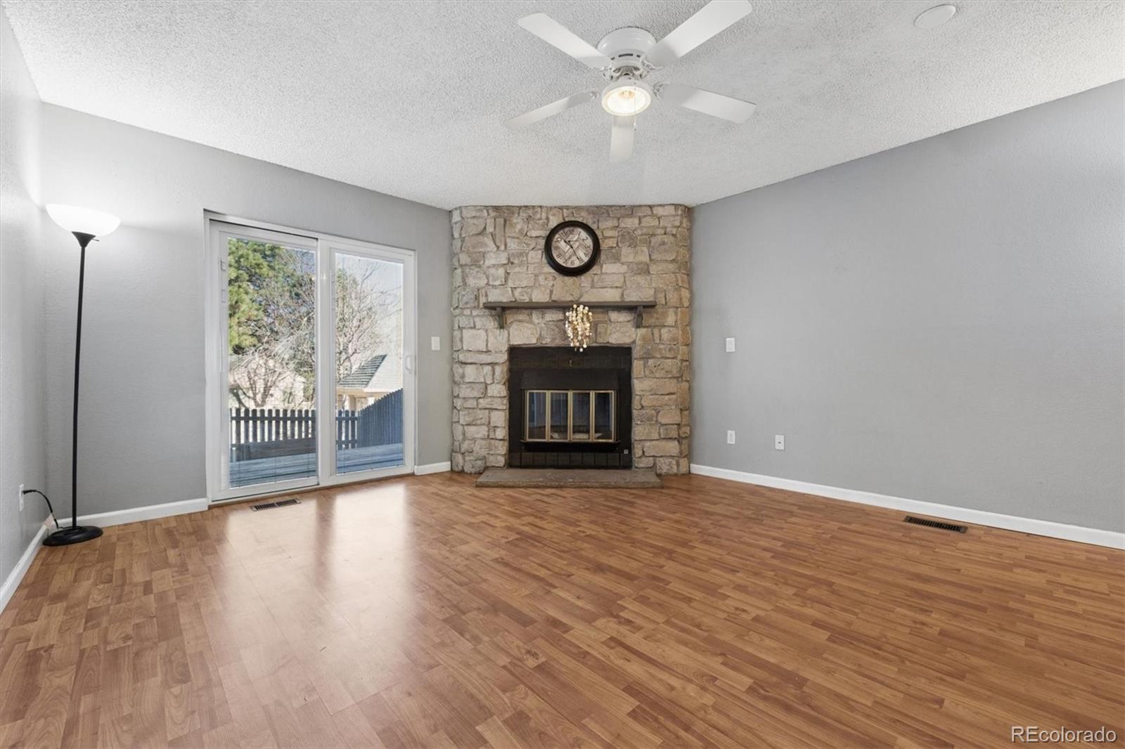 8139 South Fillmore Way Centennial, CO 80122 - Photo 2 of 29 an empty room with wooden floor a fireplace a ceiling fan and a large window