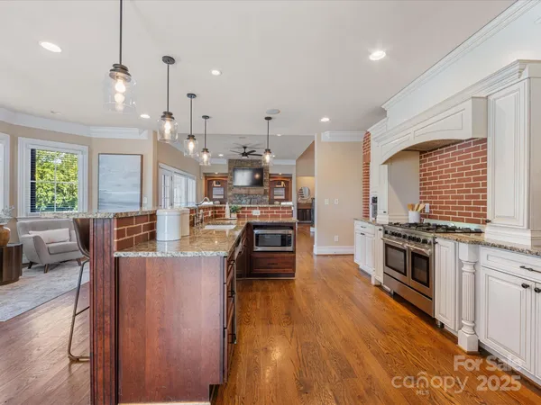 a large kitchen with stainless steel appliances granite countertop a stove a sink dishwasher a oven and a dining table with white cabinets