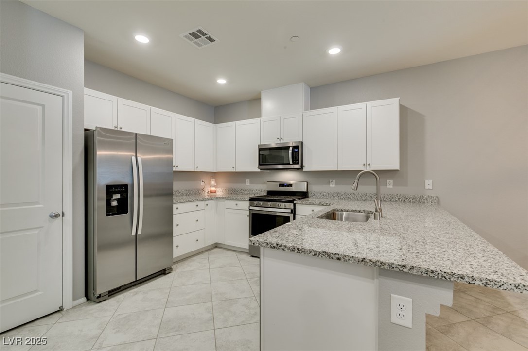 2870 Turnstone Ridge Street Henderson, NV 89044 - Photo 23 of 50 Kitchen with stainless steel appliances, a sink, a peninsula, light stone counters, and white cabinets