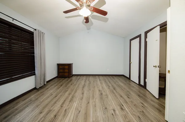 a view of an empty room with wooden floor and a ceiling fan