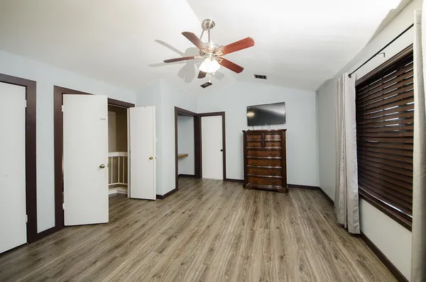 a view of an empty room with wooden floor and a ceiling fan