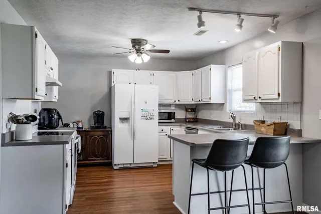 a kitchen with stainless steel appliances a stove top oven a refrigerator a sink and white cabinets with wooden floor