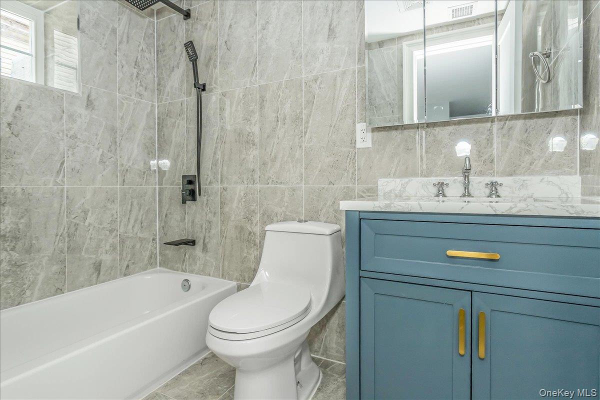 243-36 Caney Road Queens, NY 11422 - Photo 28 of 30 Full bathroom featuring bathing tub / shower combination, vanity, tile walls, and tile patterned flooring