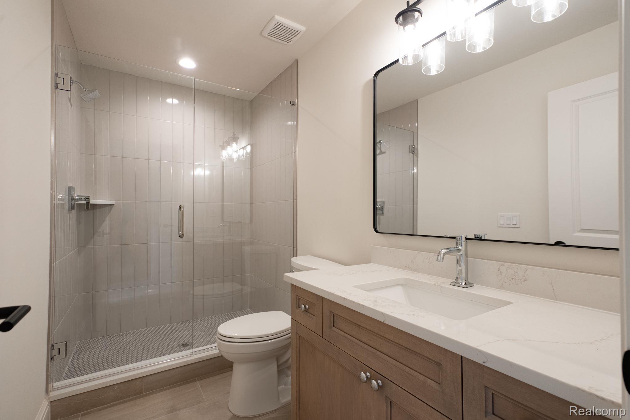 3836 Coachwood Lane Rochester, MI 48309 - Photo 67 of 82 Bathroom featuring a glass-enclosed shower, a light wood-finish vanity with a white countertop, and a contemporary mirror with overhead lighting