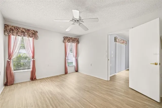 an empty room with wooden floor fan and windows