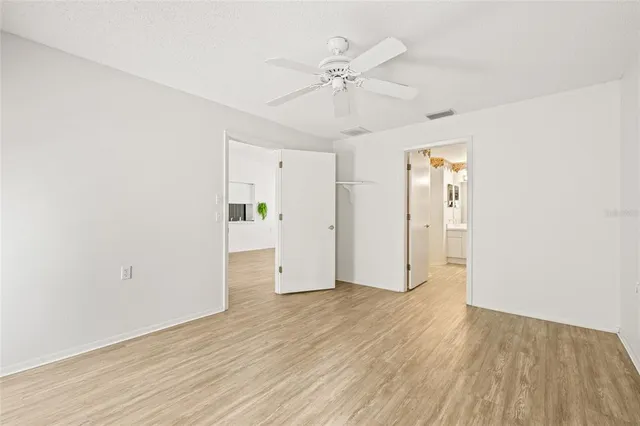 an empty room with wooden floor fan and windows