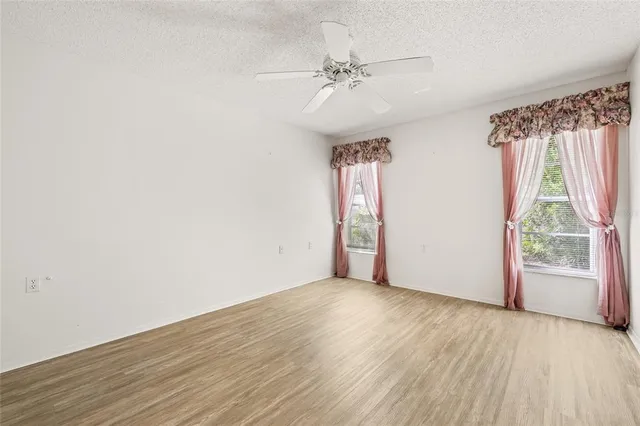 an empty room with wooden floor fan and windows