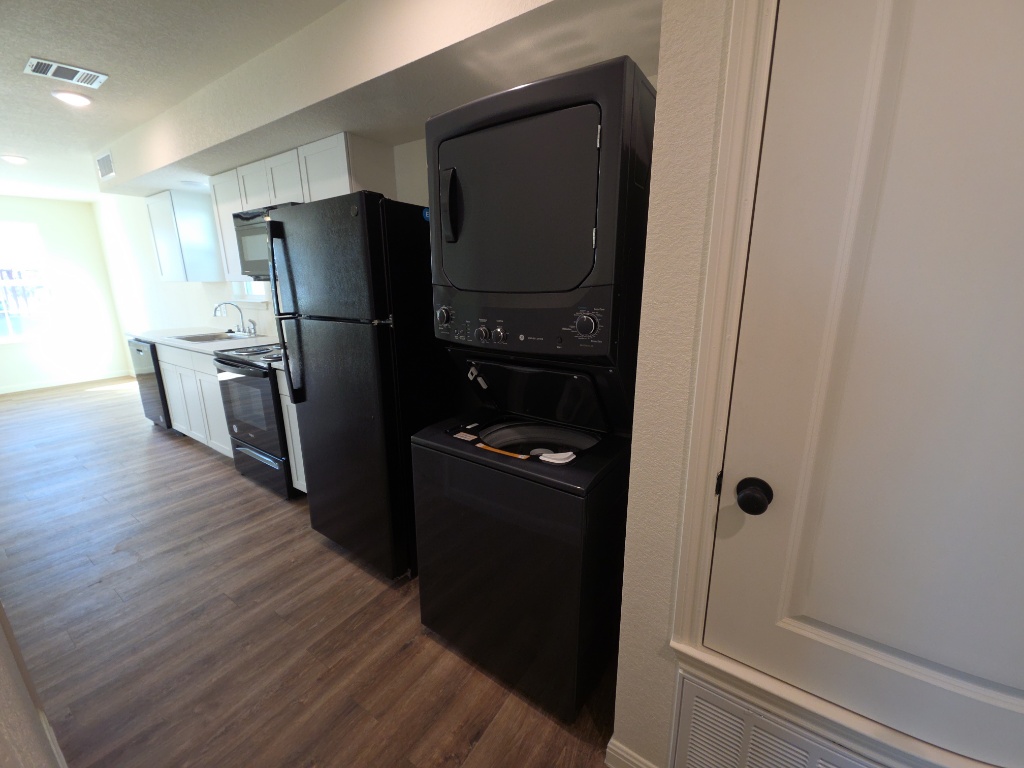 2002 West 2nd Street, Unit 100 Taylor, TX 76574 - Photo 16 of 16 Kitchen featuring white cabinets, dark wood-type flooring, black appliances, stacked washer / drying machine, and light countertops