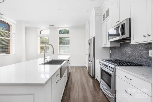 a kitchen with stainless steel appliances granite countertop a refrigerator oven a sink dishwasher and white cabinets with wooden floor