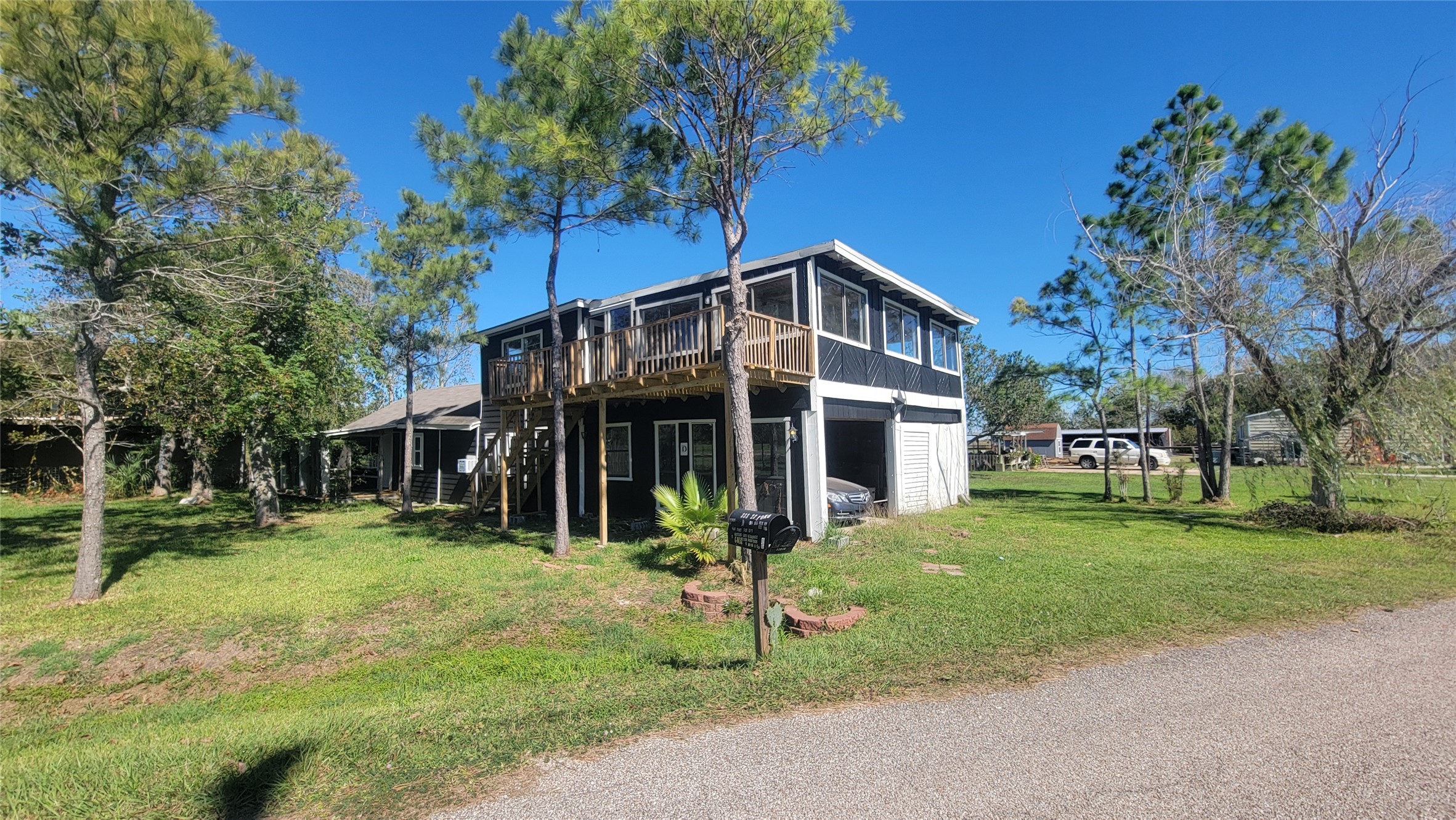 12018 Sandpiper Road Angleton, TX 77515 - Photo 42 of 48 This photo shows a two-story home with a wraparound upper deck and a screened porch below. It's surrounded by a grassy yard with trees, and has a driveway leading to a garage. The setting is tranquil, ideal for those seeking a quiet neighborhood.