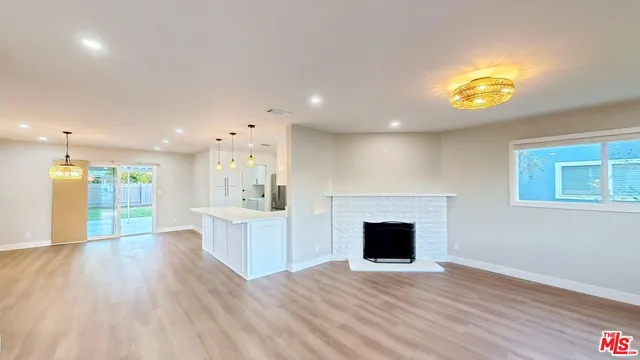 a view of an empty room with kitchen and window