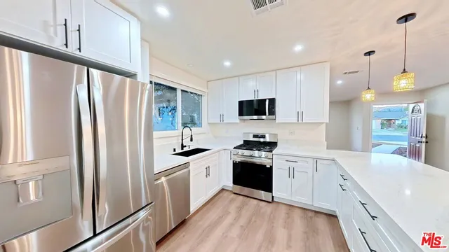 a kitchen with stainless steel appliances granite countertop a refrigerator a sink dishwasher a stove with white cabinets and wooden floor