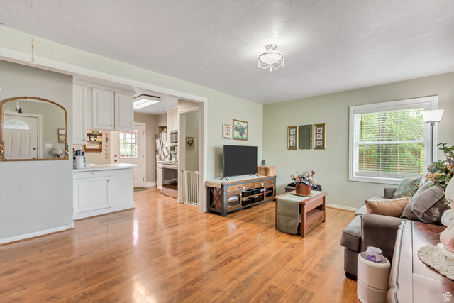 65 West 700 North Bountiful, UT 84010 - Photo 11 of 29 Hardwood-style flooring throughout the open living area, featuring a large window, light green wall tones, and an adjacent kitchen with white cabinetry