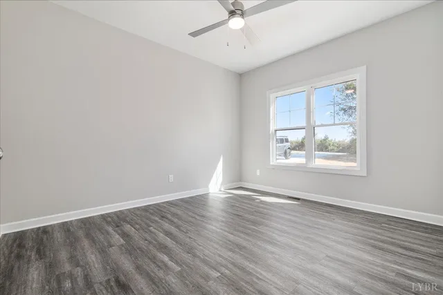 an empty room with wooden floor chandelier fan and windows