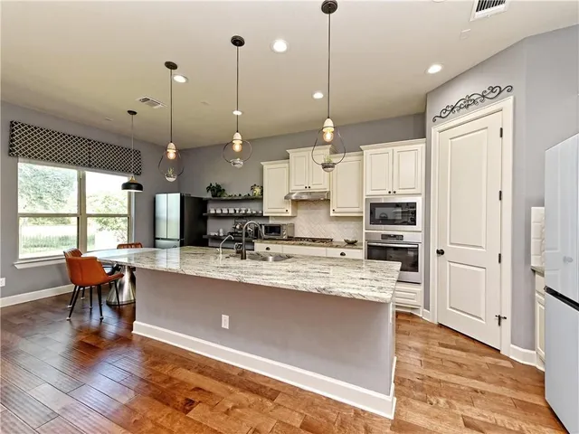 a large kitchen with stainless steel appliances kitchen island granite countertop a stove a refrigerator a oven a sink with island and chairs with wooden floor