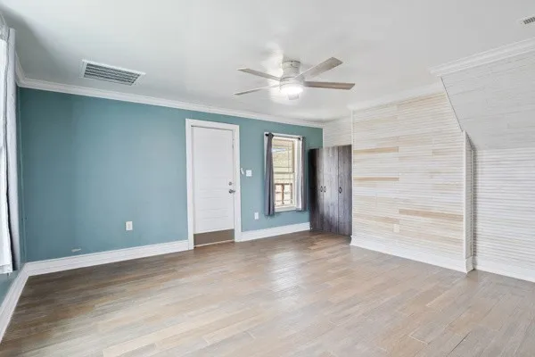 a view of an empty room with wooden floor and a ceiling fan