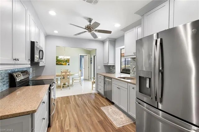 a kitchen with stainless steel appliances a refrigerator a sink dishwasher a stove and white countertops with wooden floor